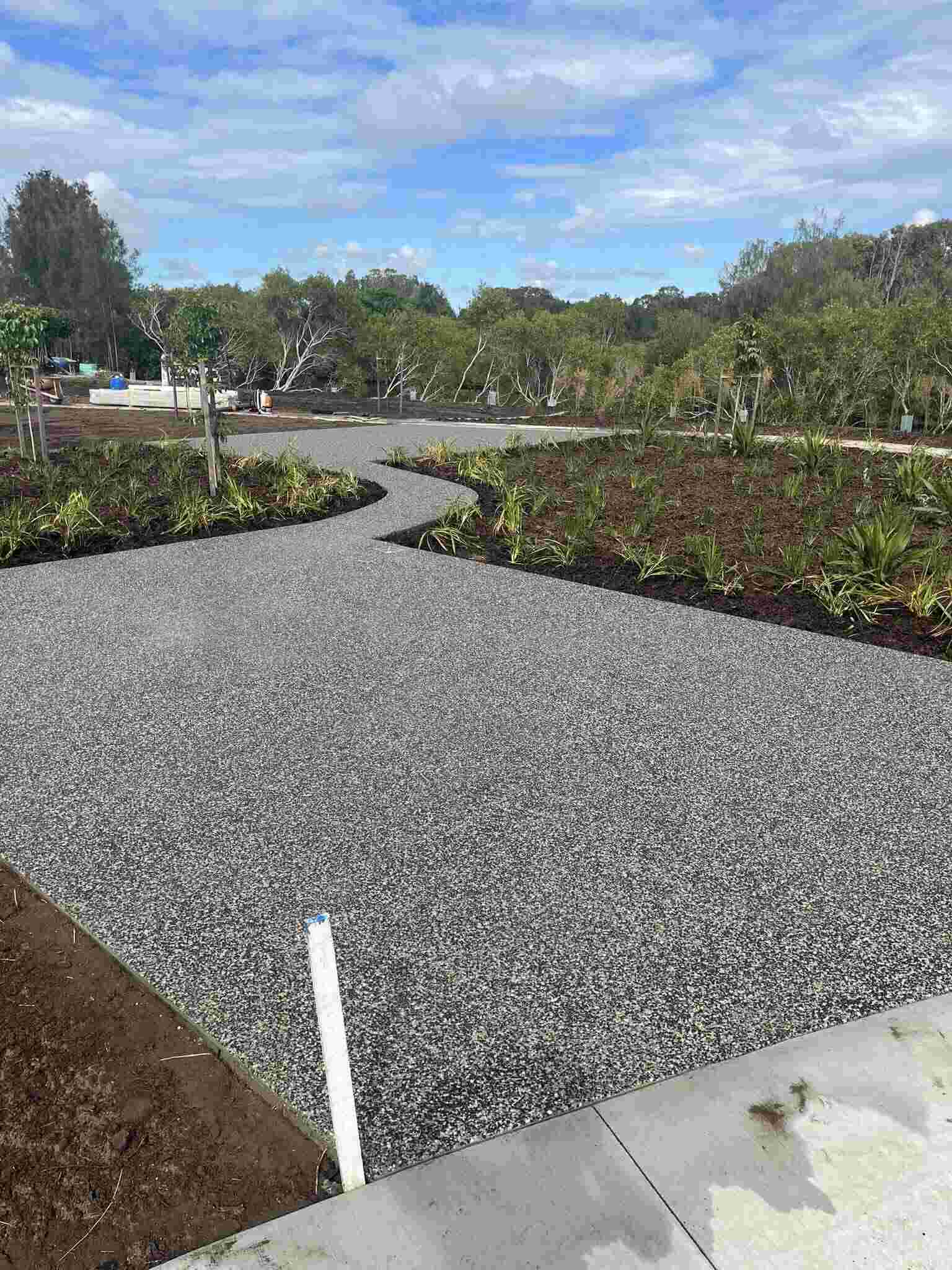 Exposed aggregate pathway winding through new garden beds
