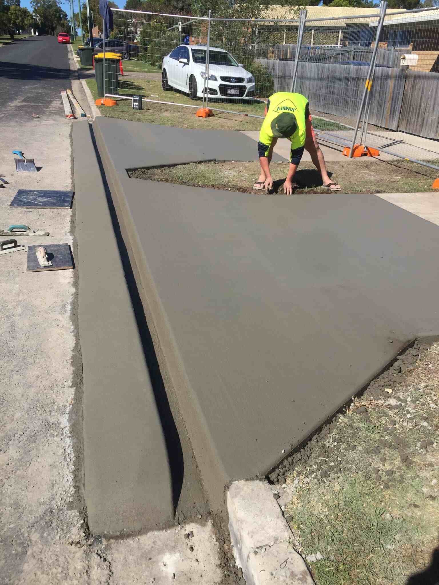 Concreter finishing a freshly poured driveway crossover beside the kerb
