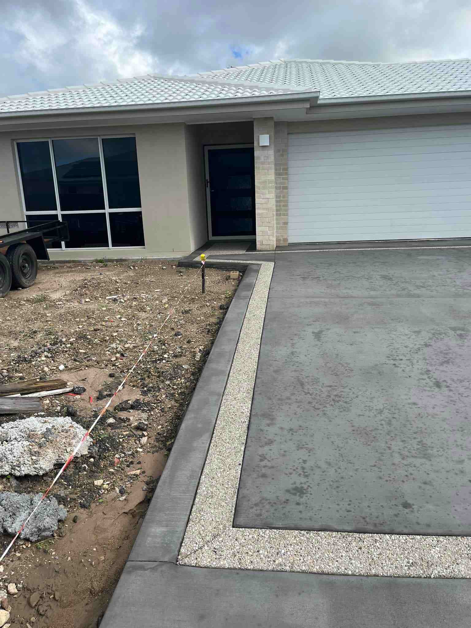 Grey concrete driveway with an exposed aggregate border leading to a garage