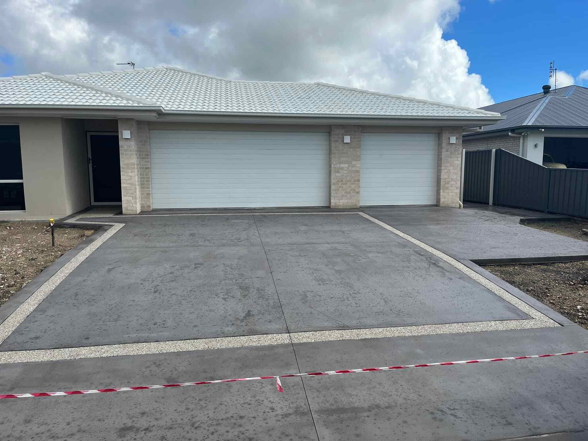 Grey concrete driveway with exposed aggregate borders in front of two garages
