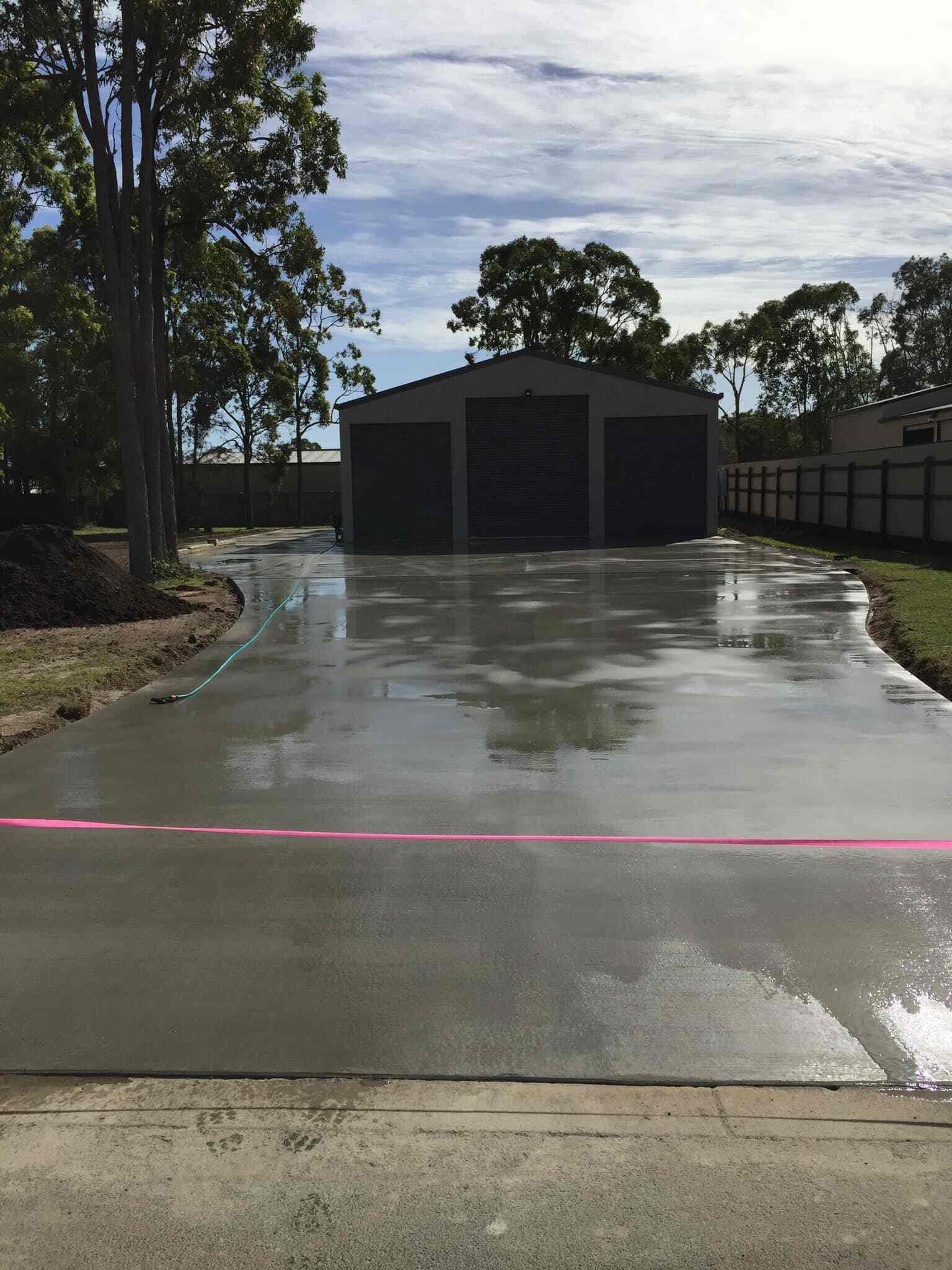 Freshly poured wet concrete driveway leading to a large dark shed