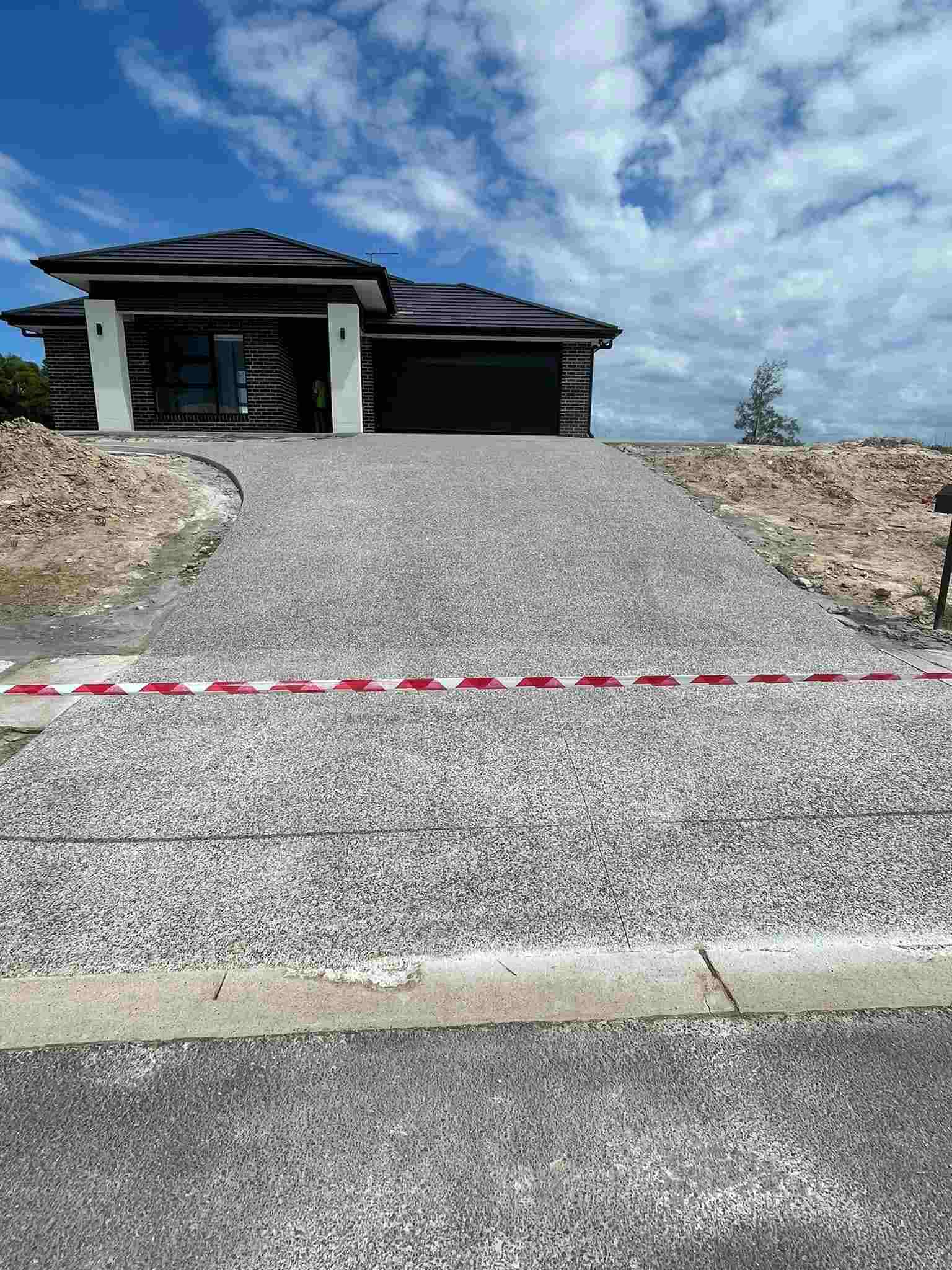 Long concrete driveway leading up to a new home with a dark roof