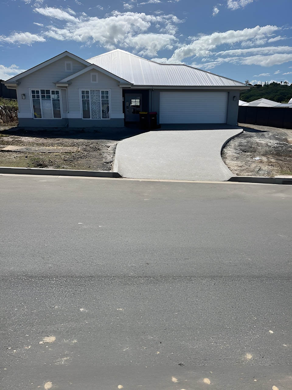 New concrete driveway and kerb in front of a grey home with a white roof