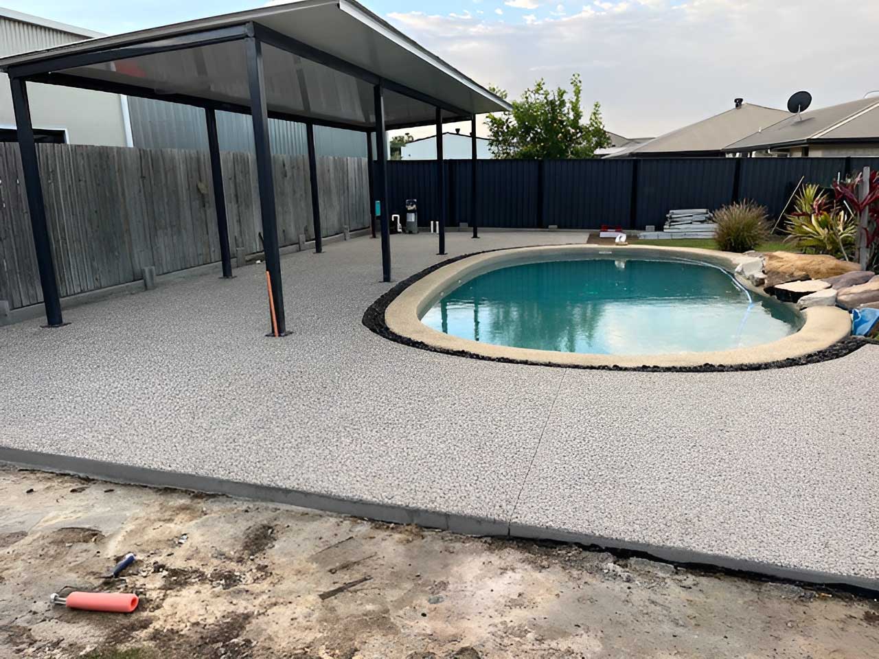 Exposed aggregate pool surround partly covered by a steel-framed shade roof