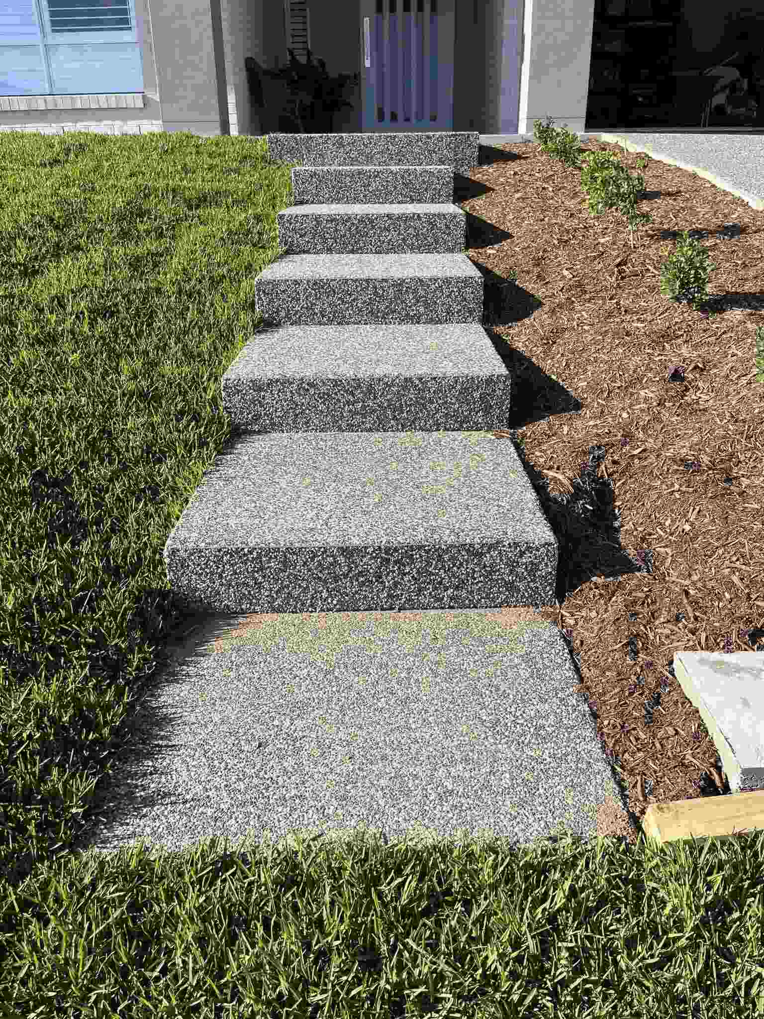 Exposed aggregate steps leading up to a front door between lawn and garden