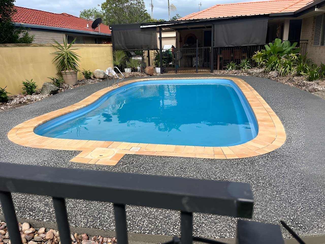 Kidney-shaped pool with orange coping and an exposed aggregate surround, wide view