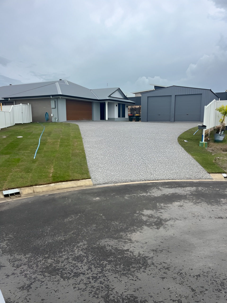 Exposed aggregate driveway leading to a house and a large double shed