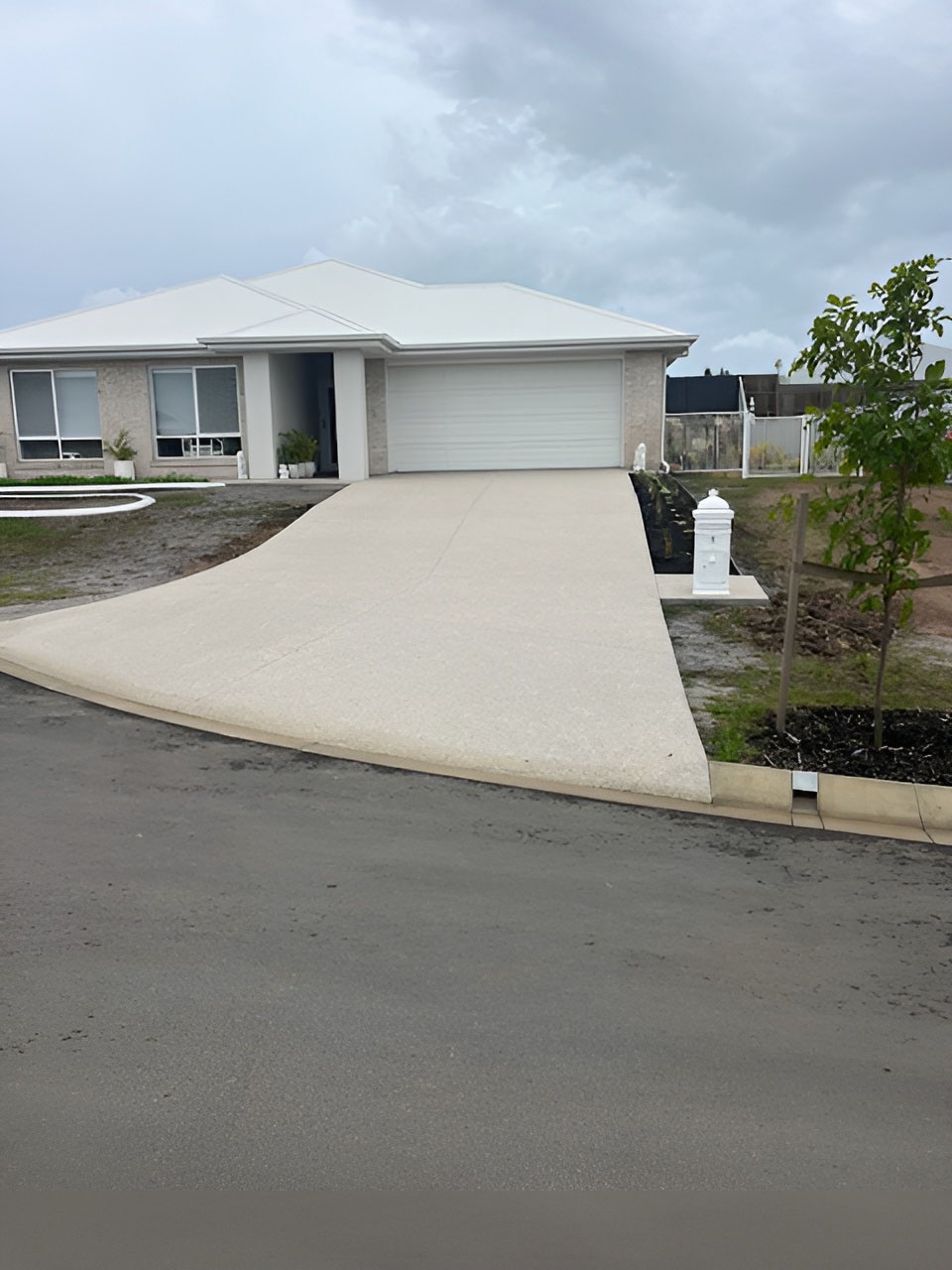 Plain concrete driveway curving up to a new home with a white garage door, tall view