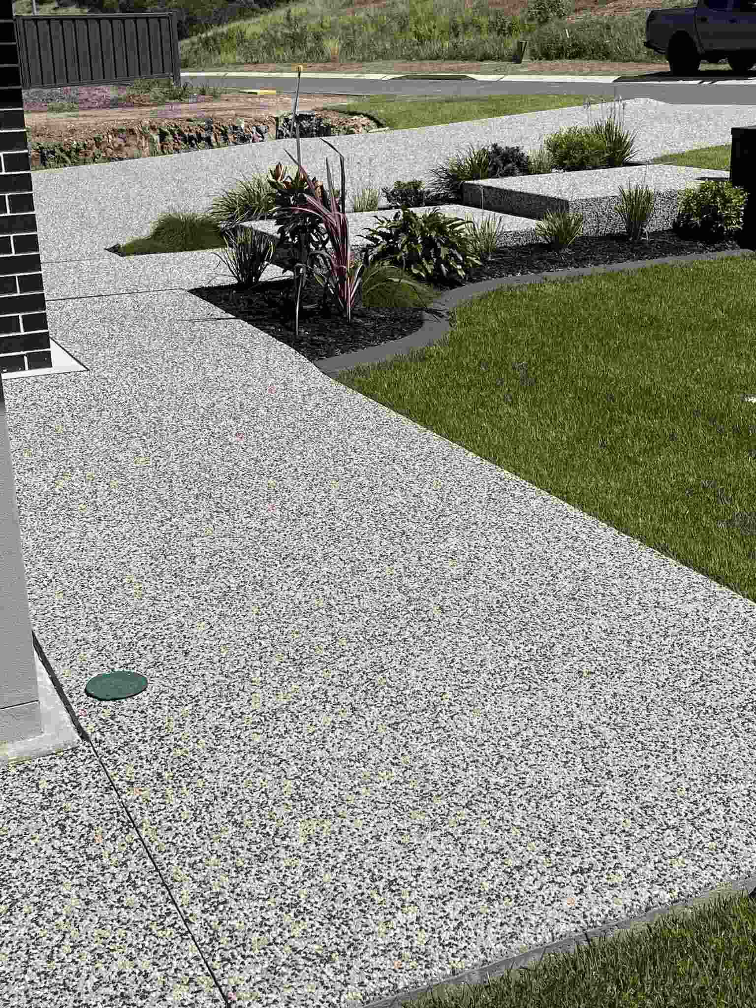 Exposed aggregate path running beside a lawn and garden bed along a house