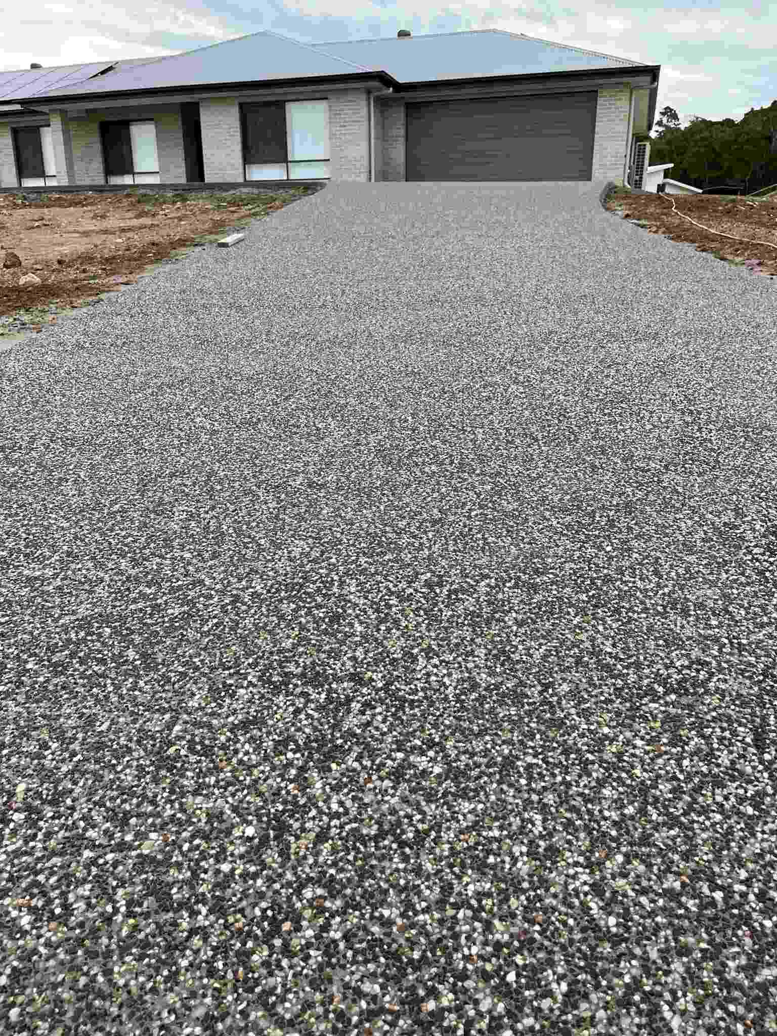 Exposed aggregate driveway leading to a brick home with a dark garage door
