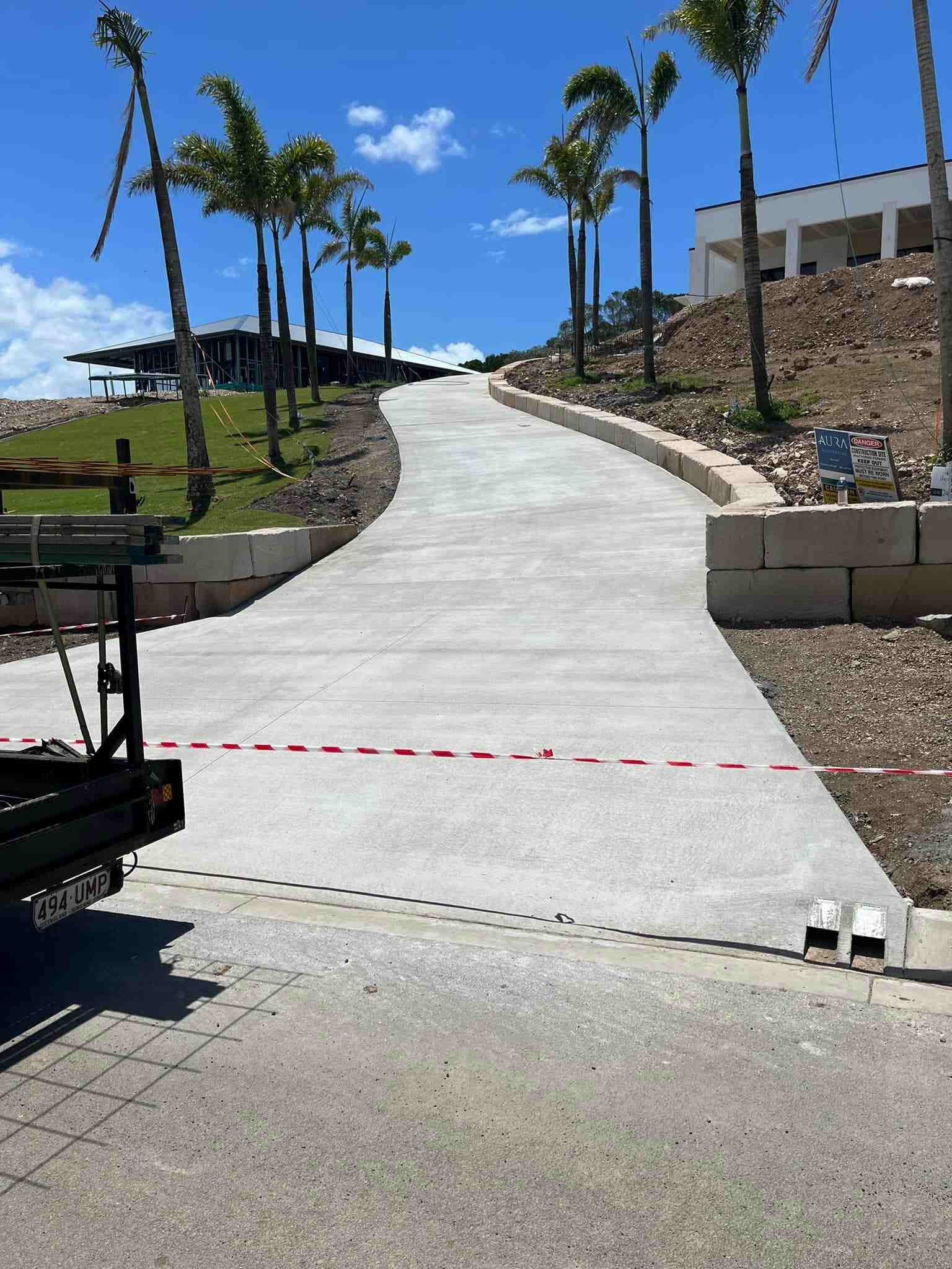 Curved concrete driveway between block retaining walls, palm trees on the slope