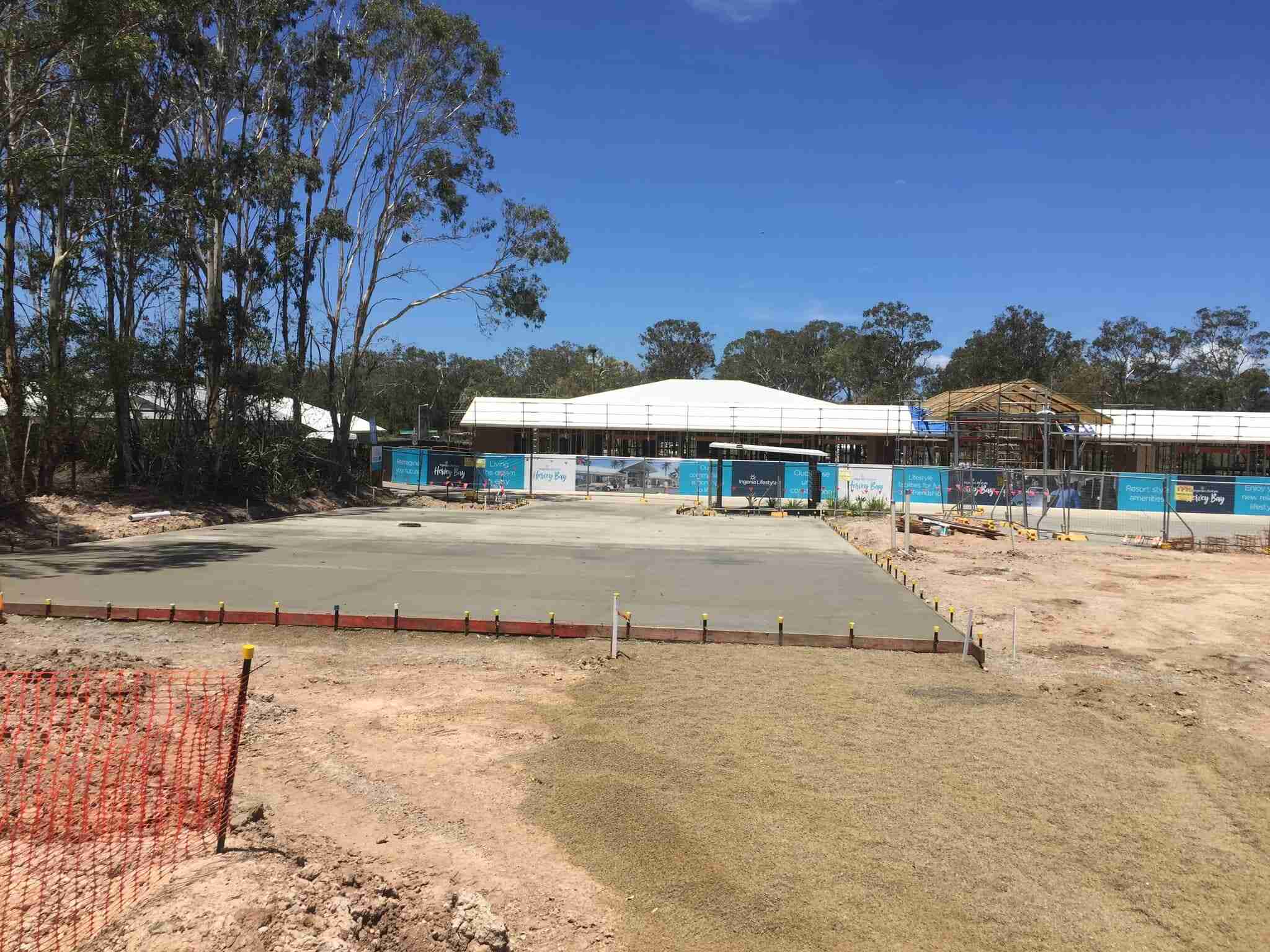 Concrete slab with timber formwork on a cleared site behind orange safety fencing