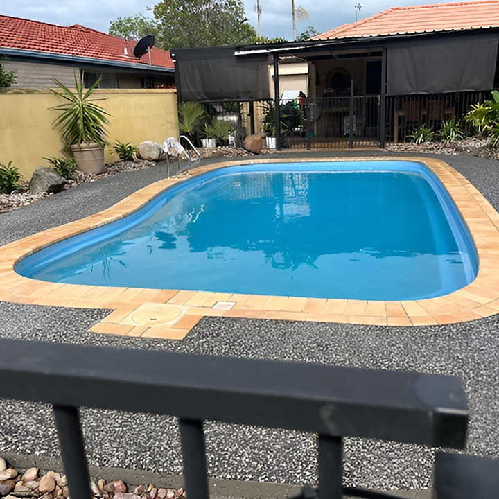 Kidney-shaped pool with orange coping and an exposed aggregate surround